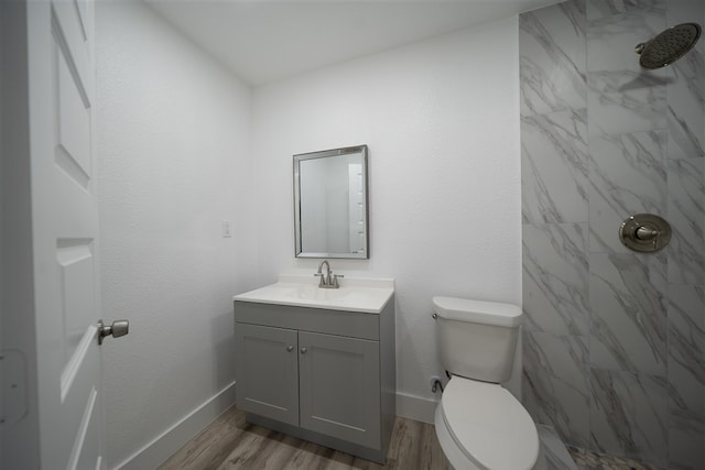 full bathroom featuring baseboards, toilet, wood finished floors, a tile shower, and vanity