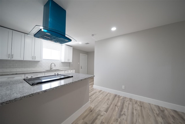 kitchen featuring light stone counters, island exhaust hood, backsplash, white cabinetry, and a sink