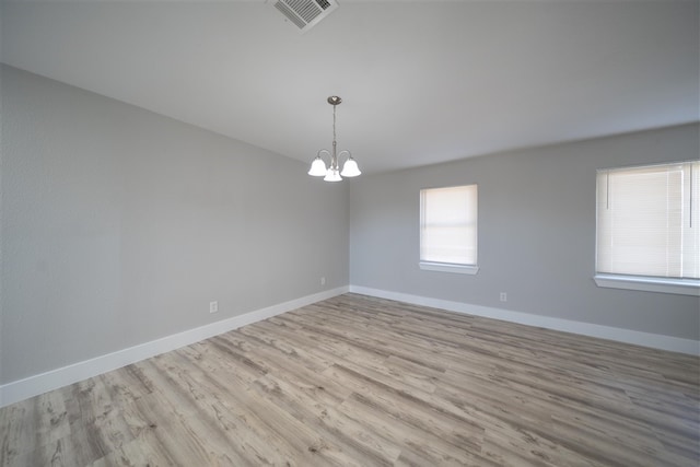 empty room featuring visible vents, a notable chandelier, baseboards, and wood finished floors