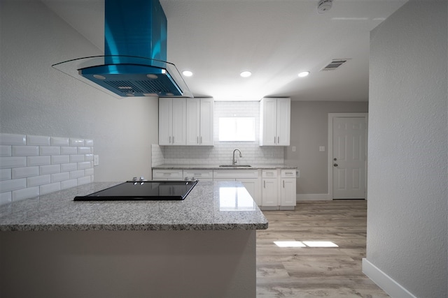 kitchen with visible vents, white cabinets, island range hood, decorative backsplash, and light wood-style floors