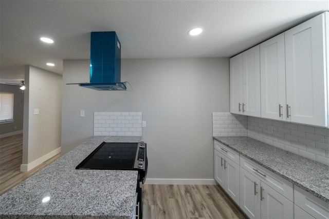 kitchen featuring light stone counters, tasteful backsplash, light wood-style floors, white cabinetry, and exhaust hood