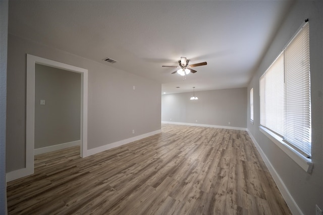 empty room featuring ceiling fan with notable chandelier, wood finished floors, visible vents, and baseboards