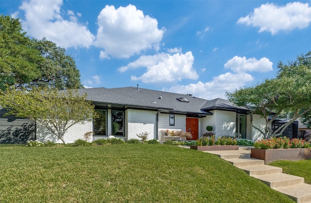 rear view of property featuring brick siding, a lawn, and a shingled roof