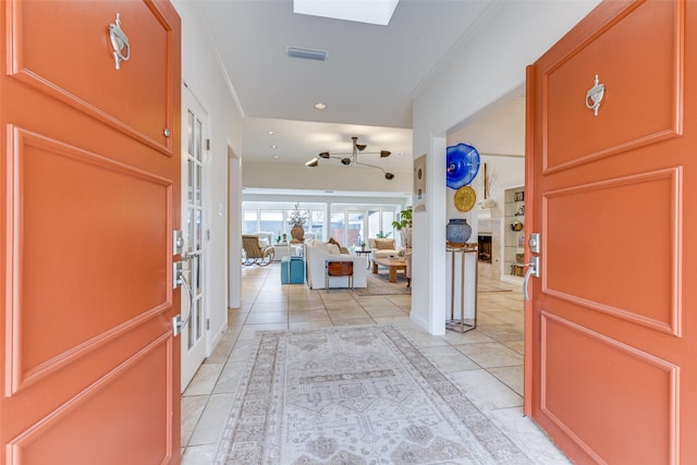 foyer entrance featuring a skylight, a fireplace, visible vents, ornamental molding, and light tile patterned flooring