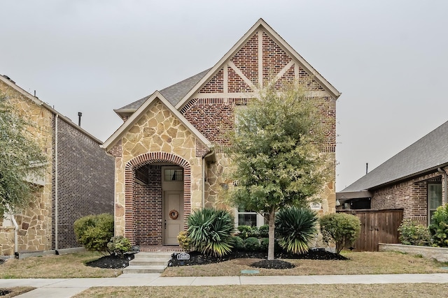 english style home featuring stone siding, brick siding, and fence