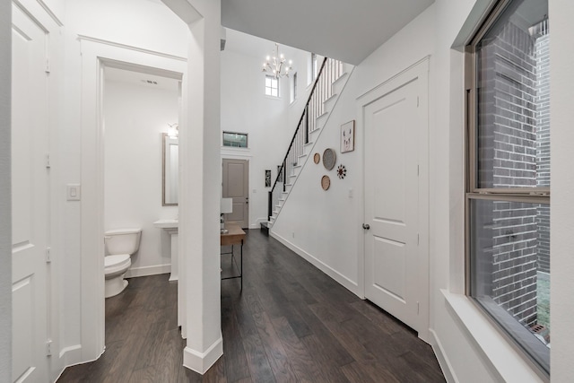 hallway featuring a chandelier, dark wood finished floors, baseboards, and stairs