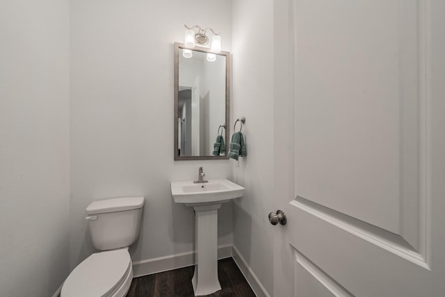 half bath with toilet, a sink, baseboards, and wood finished floors