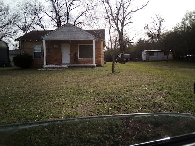 bungalow-style home featuring covered porch, a storage unit, a front lawn, and an outbuilding