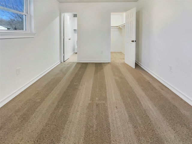 unfurnished bedroom featuring ensuite bath, a spacious closet, and baseboards