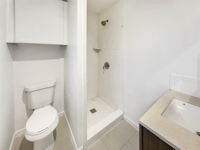 full bathroom featuring toilet, baseboards, a tile shower, and vanity