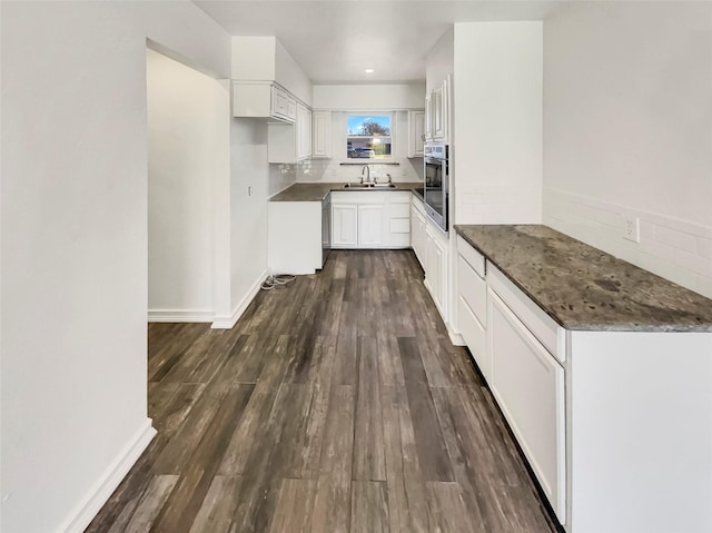 kitchen featuring baseboards, dark wood-type flooring, oven, white cabinetry, and a sink