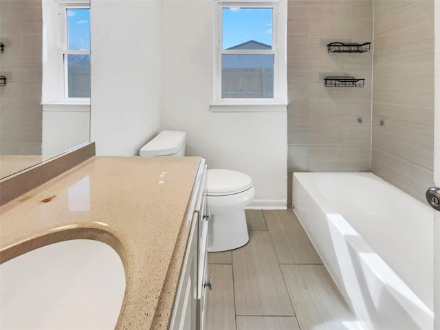 bathroom featuring a wealth of natural light, a tub to relax in, vanity, and toilet