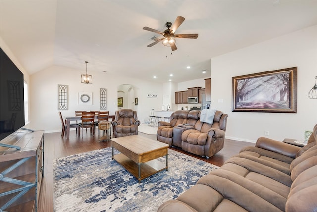 living room featuring arched walkways, ceiling fan, wood finished floors, baseboards, and vaulted ceiling