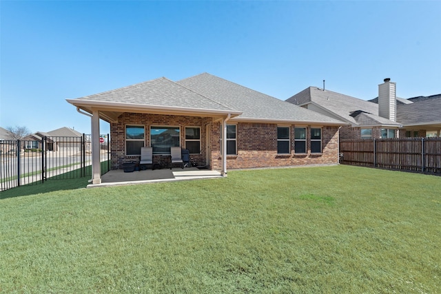 rear view of property with brick siding, a fenced backyard, a lawn, and roof with shingles