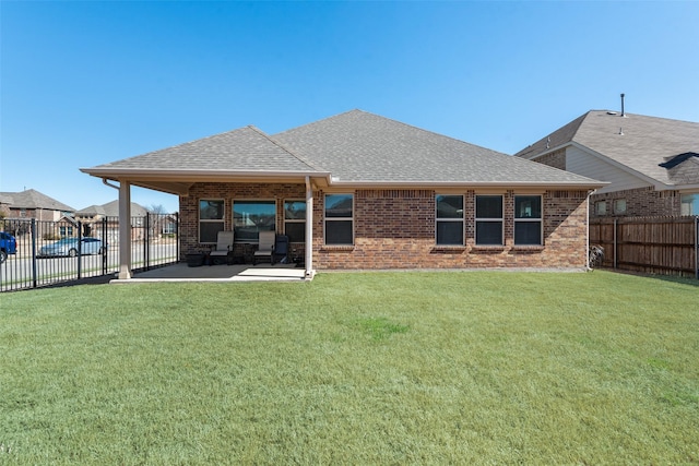 back of house featuring a patio, roof with shingles, fence, a yard, and brick siding