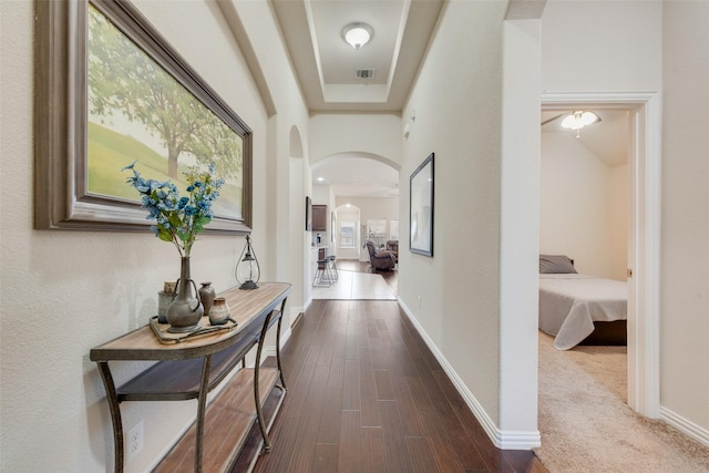 corridor featuring dark wood-style floors, arched walkways, visible vents, and baseboards