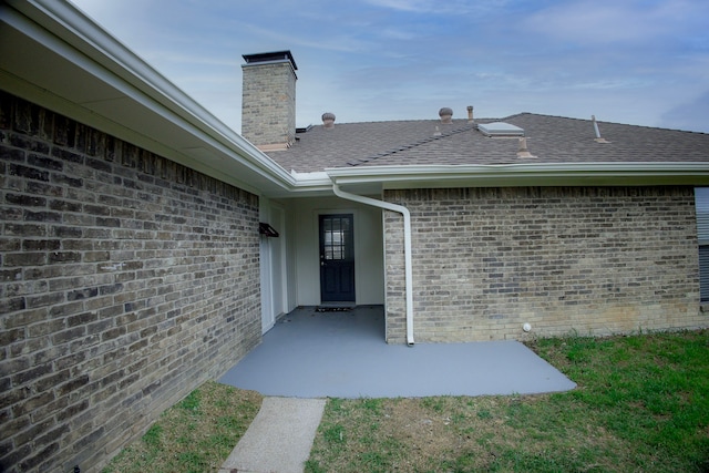 view of exterior entry with a shingled roof, brick siding, and a chimney