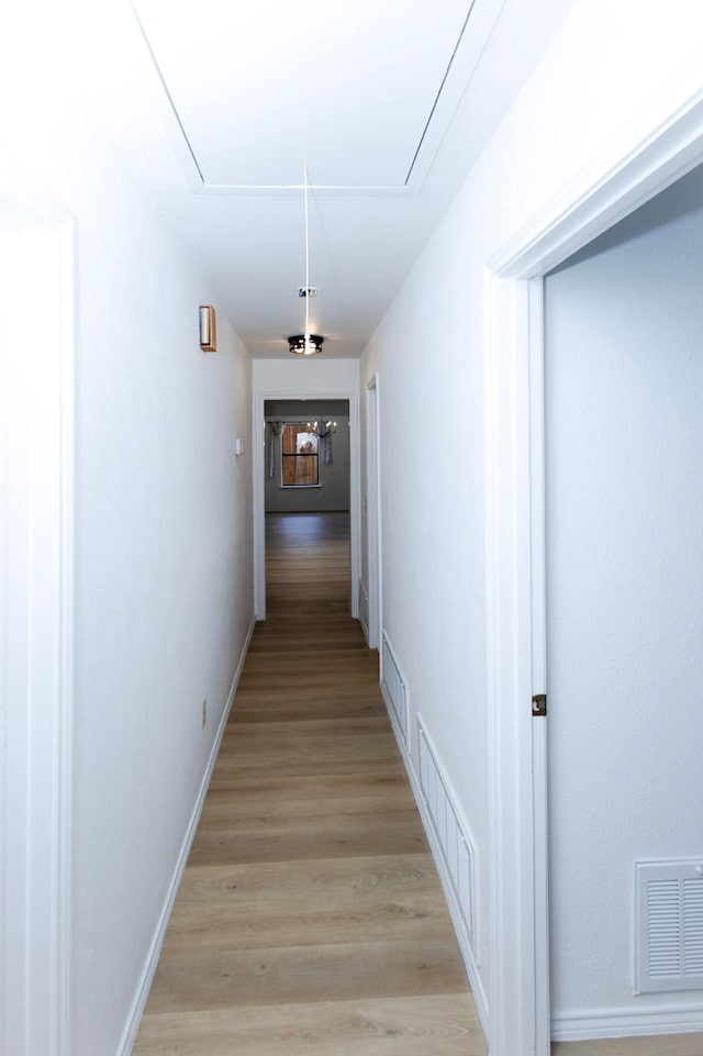 corridor featuring light wood-style floors, attic access, visible vents, and baseboards