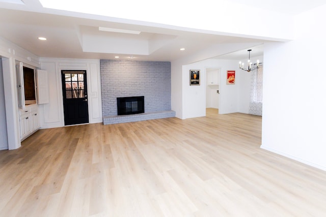 unfurnished living room with baseboards, an inviting chandelier, light wood-style floors, a fireplace, and recessed lighting