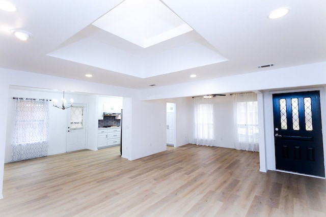 entryway with visible vents, light wood-style flooring, a tray ceiling, a chandelier, and recessed lighting