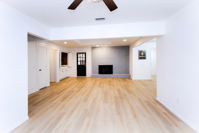 unfurnished living room with visible vents, baseboards, ceiling fan, light wood-type flooring, and a brick fireplace