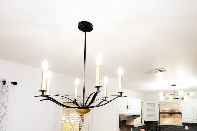 room details featuring under cabinet range hood, a notable chandelier, white cabinetry, a kitchen breakfast bar, and visible vents