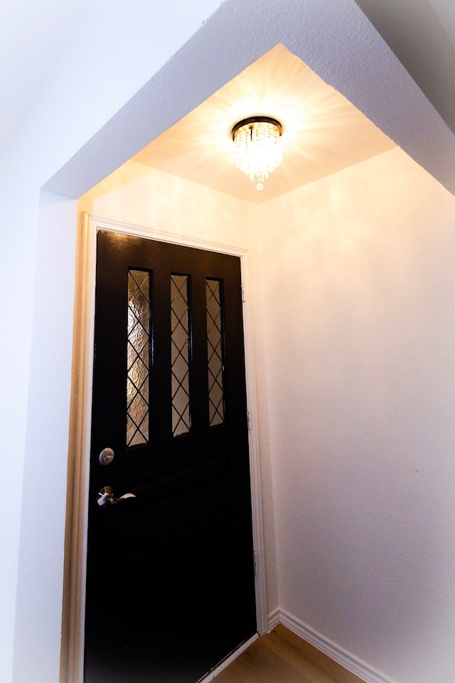 foyer with wood finished floors, baseboards, and an inviting chandelier