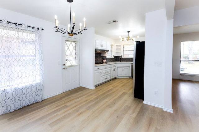 kitchen featuring under cabinet range hood, visible vents, white cabinets, freestanding refrigerator, and an inviting chandelier