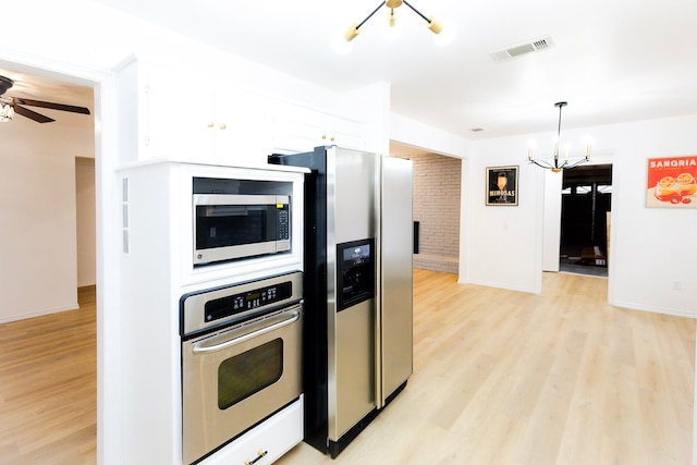 kitchen with light wood finished floors, stainless steel appliances, visible vents, white cabinets, and ceiling fan with notable chandelier