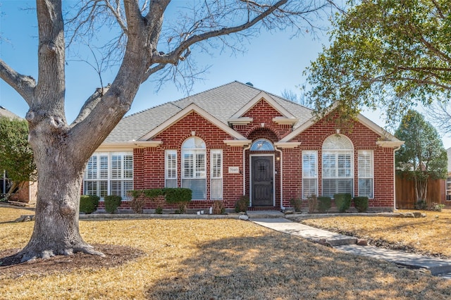 view of front of property with brick siding, a front lawn, and a shingled roof