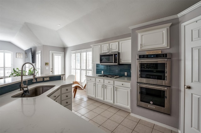 kitchen featuring lofted ceiling, appliances with stainless steel finishes, a healthy amount of sunlight, light tile patterned flooring, and a sink