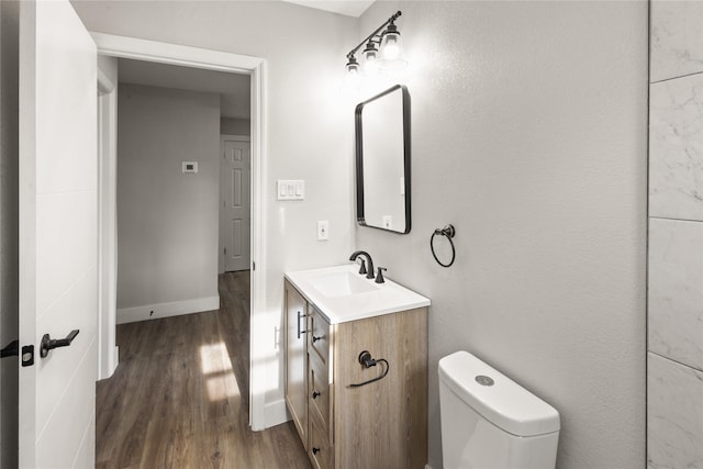 half bathroom featuring baseboards, vanity, toilet, and wood finished floors