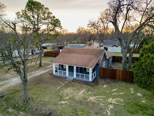 rear view of property featuring a yard, a porch, roof with shingles, and fence