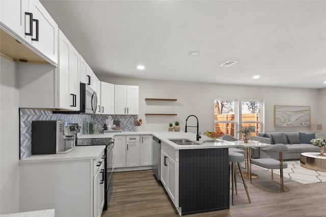 kitchen with a breakfast bar, open shelves, appliances with stainless steel finishes, a sink, and a peninsula