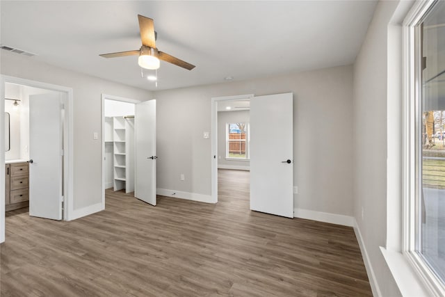 unfurnished bedroom with ensuite bathroom, wood finished floors, visible vents, baseboards, and a spacious closet