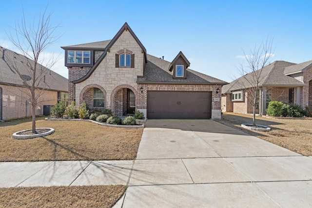 french country home featuring a garage, brick siding, a shingled roof, driveway, and stone siding