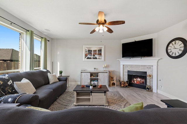 living room with a fireplace, visible vents, ceiling fan, wood finished floors, and baseboards