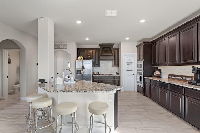 kitchen featuring visible vents, custom range hood, a breakfast bar area, stainless steel appliances, and a sink