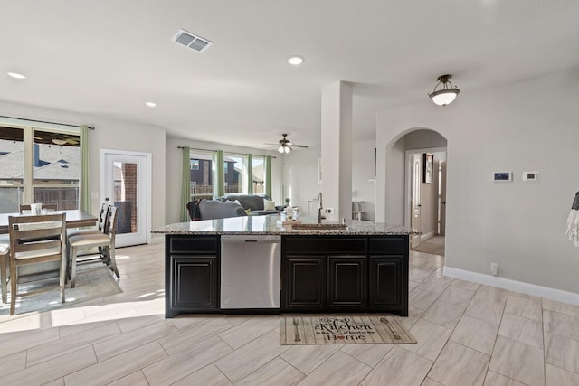 kitchen featuring visible vents, arched walkways, dishwasher, light stone countertops, and a sink