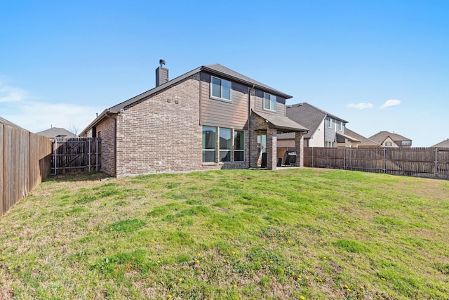 rear view of house featuring brick siding, a yard, a chimney, and a fenced backyard