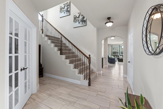 entryway with arched walkways, french doors, stairway, and baseboards