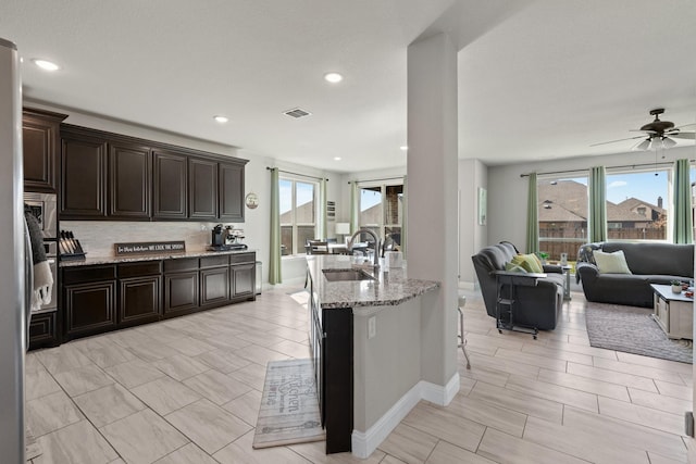 kitchen featuring tasteful backsplash, visible vents, open floor plan, a sink, and light stone countertops