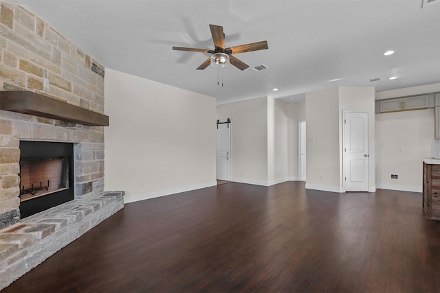 unfurnished living room featuring a barn door, a fireplace, wood finished floors, visible vents, and a ceiling fan