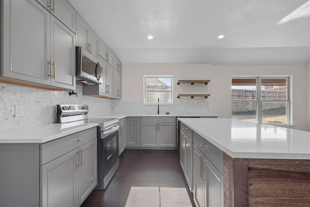 kitchen with stainless steel appliances, a sink, light countertops, gray cabinets, and open shelves