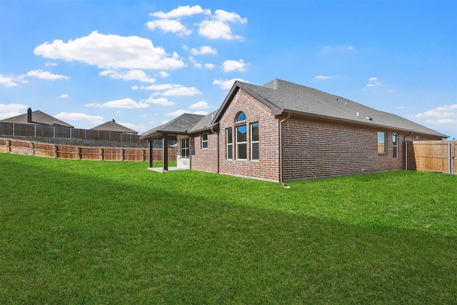 back of house featuring a shingled roof, a lawn, fence, a patio area, and brick siding