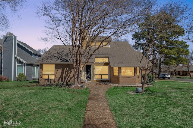 view of front of home featuring a yard, a shingled roof, and brick siding