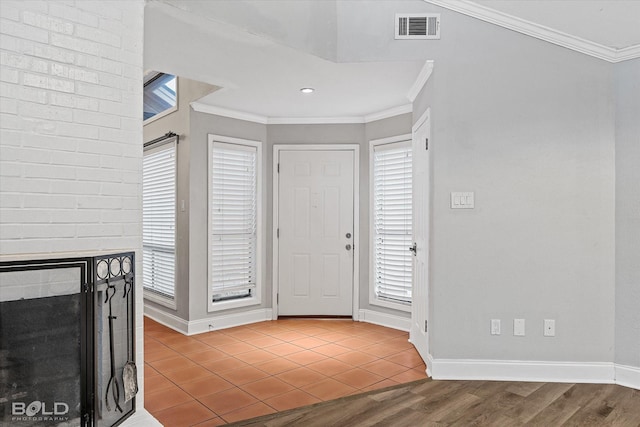 foyer featuring baseboards, a brick fireplace, visible vents, and crown molding