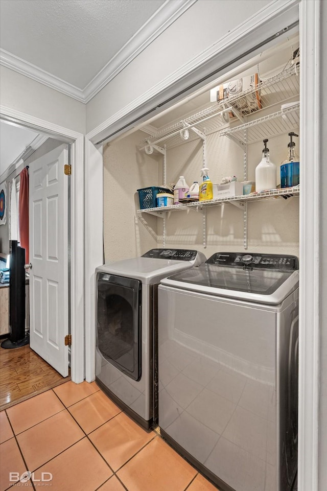 clothes washing area featuring light tile patterned floors, laundry area, ornamental molding, and washer and clothes dryer