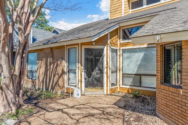 property entrance featuring brick siding and roof with shingles