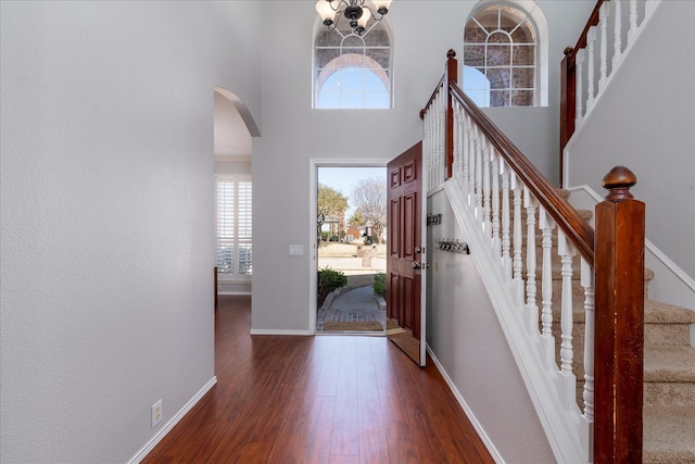 foyer with arched walkways, dark wood-type flooring, a towering ceiling, baseboards, and stairway